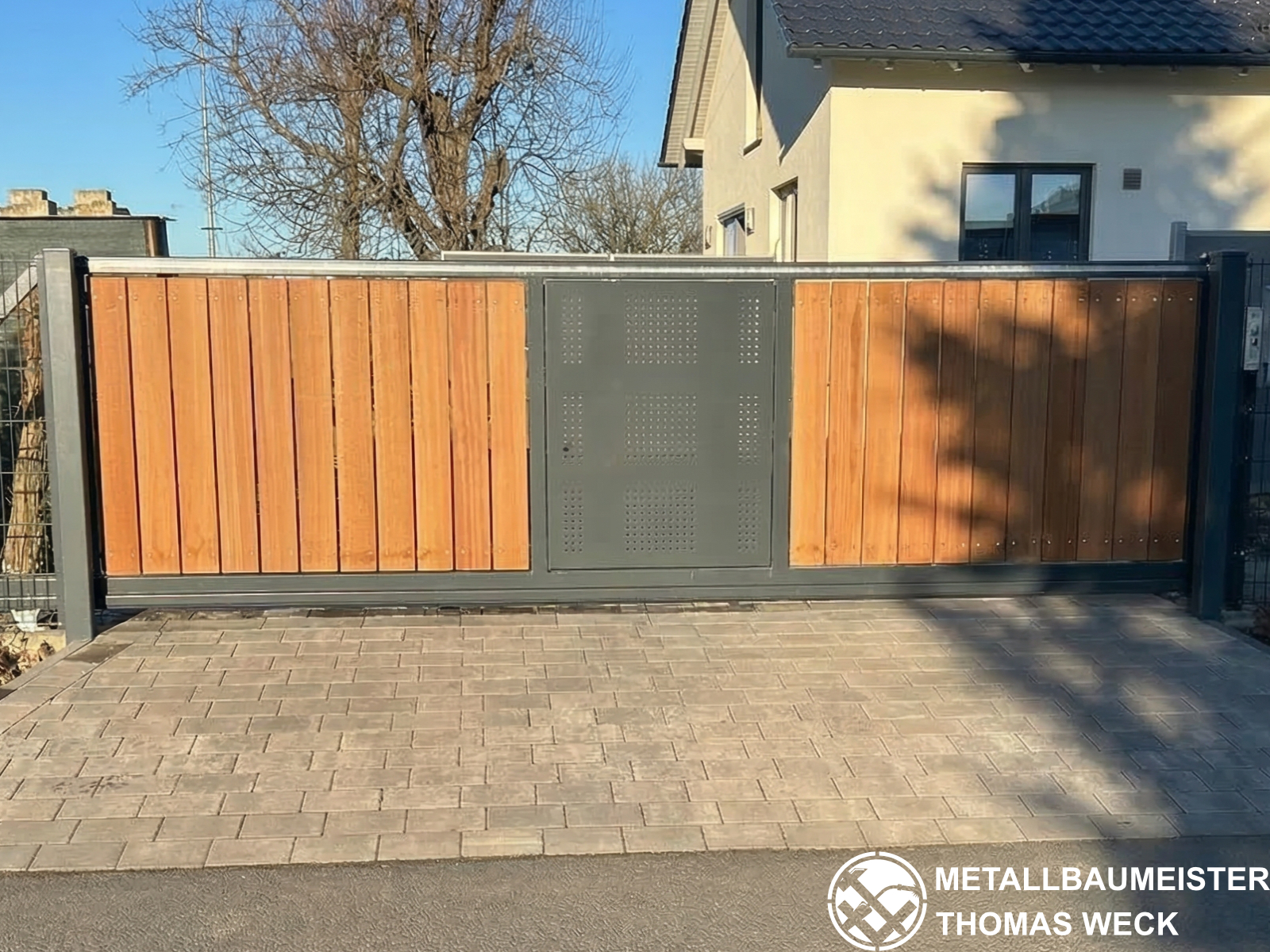 Einfahrtstor kombiniert aus anthrazitfarbenem Metallrahmen und vertikalen Holzlatten-Füllungen